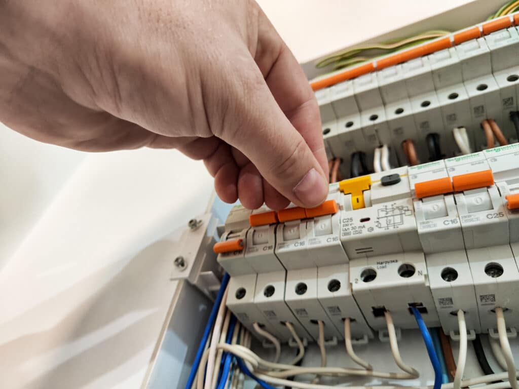 Actionnement disjoncteur différentiel Schneider tableau élec Main actionnant le levier orange d'un disjoncteur différentiel Schneider C25, 30 mA, dans un tableau électrique.